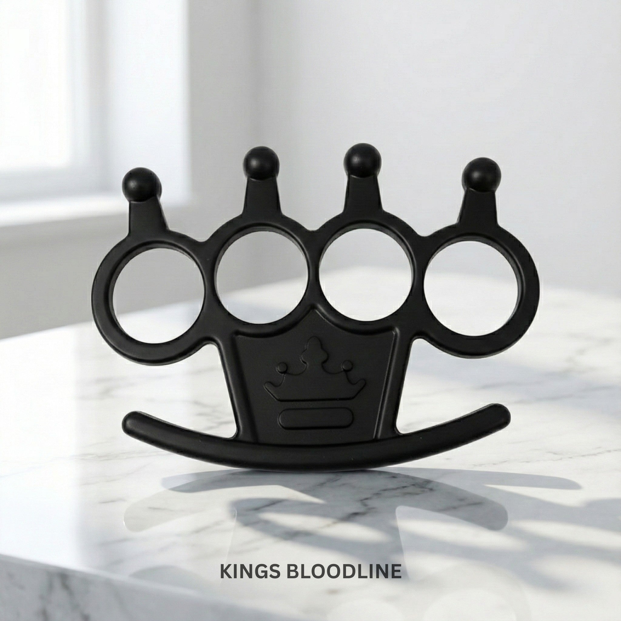 Black knuckle duster with a crown emblem on a marble surface, branded 'Kings Bloodline'.